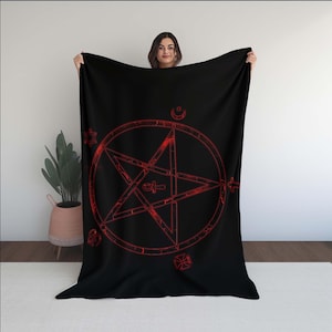 May include: Black blanket featuring a red pentagram design with various symbols. The blanket is held up, showcasing the large, central star within a circle, and other geometric shapes. The design is a bold, eye-catching statement piece.