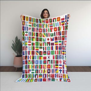 Può includere: Una coperta bianca con un motivo ripetuto di bandiere quadrate di diversi paesi. Le bandiere sono disposte a griglia, mostrando una varietà di simboli nazionali. La coperta è tenuta in mano, mostrando il suo design completo.