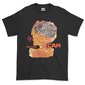 Può includere: T-shirt nera con un design grafico colorato. Il design presenta un profilo umano stilizzato con un motivo a forma di cervello e la parola "CAN" in arancione. È presente anche il testo "TAGO MAGO".