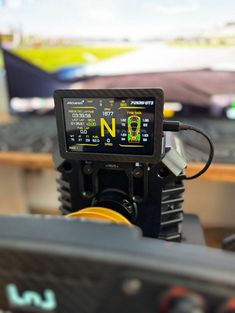 May include: A black digital display screen with the text "McLaren" and "720S GT3" at the top. The screen shows race data, including lap times, RPM, and tire data. The screen is mounted on a black device.
