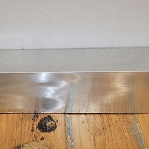 Könnte beinhalten: Ein rechteckiges Regal aus silbernem Metall mit gebürsteter Oberfläche.