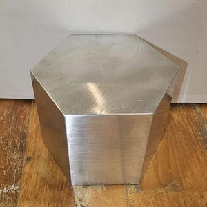 Pode incluir: Uma caixa hexagonal prateada com um acabamento liso e escovado.