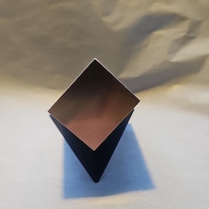 Pode incluir: Uma pirâmide geométrica preta com uma superfície reflexiva.