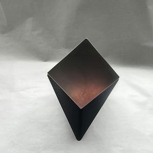 Op de afbeelding: Een geometrisch gevormde metalen vaas in zwart en zilver met een diamantvormige opening.