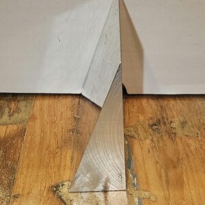 Pode incluir: Um prisma triangular prateado com uma superfície reflexiva. O prisma está em pé sobre um piso de madeira.