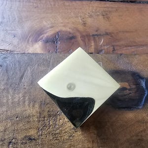 Könnte beinhalten: Ein glänzender, diamantförmiger Dekorknopf in Gold.