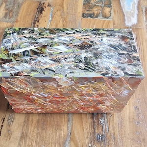 Pode incluir: Uma caixa retangular com um design abstrato e colorido. A caixa é feita de um material que parece ser resina ou plástico. O design apresenta uma mistura de cores prata, dourado, verde e vermelho.