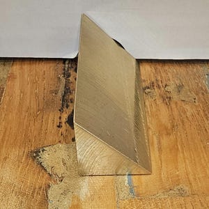Pode incluir: Um bloco de latão de forma triangular com uma superfície texturizada.