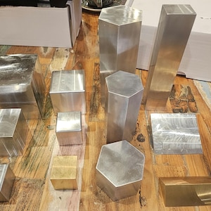 May include: A collection of silver and gold metal display stands of various shapes and sizes. The stands are arranged on a wooden surface.