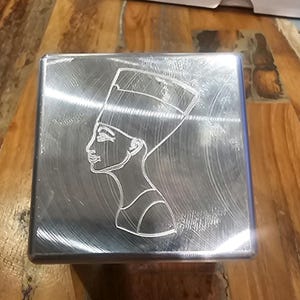 Könnte beinhalten: Eine silberne Metallbox mit einem gravierten Bild einer ägyptischen Königin, die eine Kopfbedeckung trägt.