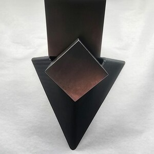 May include: A black triangular stand with a copper-colored square prism on top. The prism is sitting on a black rectangular base.