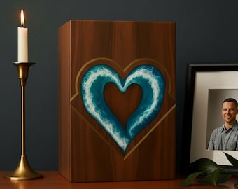 May include: A wooden urn with a heart-shaped design featuring blue and white waves. The urn is displayed on a wooden surface with a lit candle in a gold candlestick and a framed photograph.