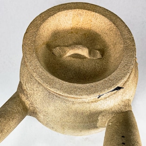 May include: A beige ceramic teapot with two spouts and a lid. The teapot has a textured surface and a handle on the lid.