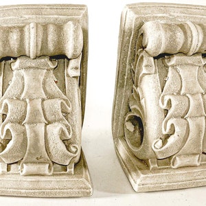 Peut inclure: Une paire de corbeaux en plâtre blanc ornés de volutes complexes et d'une bande décorative en haut.