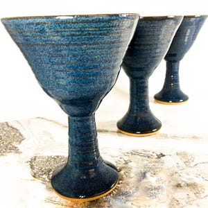 May include: Three blue ceramic goblets with a textured, striped design. The goblets have a wide bowl and a tall, slender stem.