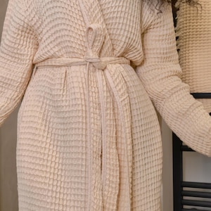 May include: A cream-colored waffle weave robe with a self-tie belt. The robe is made of a soft, absorbent material and is perfect for lounging around the house.