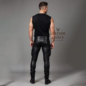 May include: A person wearing black leather trousers with cargo pockets and a black sleeveless top. The trousers have a slim fit and are made from soft, supple leather. The top is a simple, classic design. The person is standing with their back to the camera. The image is from Leather and Legacy, a company that specialises in premium leather goods.
