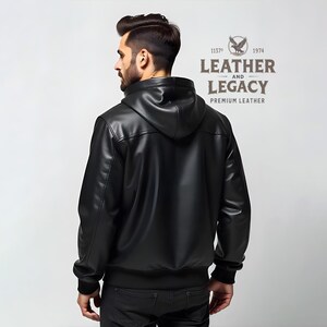 May include: Black leather jacket with a hood. The jacket has a zipper closure and a ribbed knit collar, cuffs, and waistband. The back of the jacket features a stitched detail. The jacket has the text "Leather and Legacy Premium Leather" on the back.