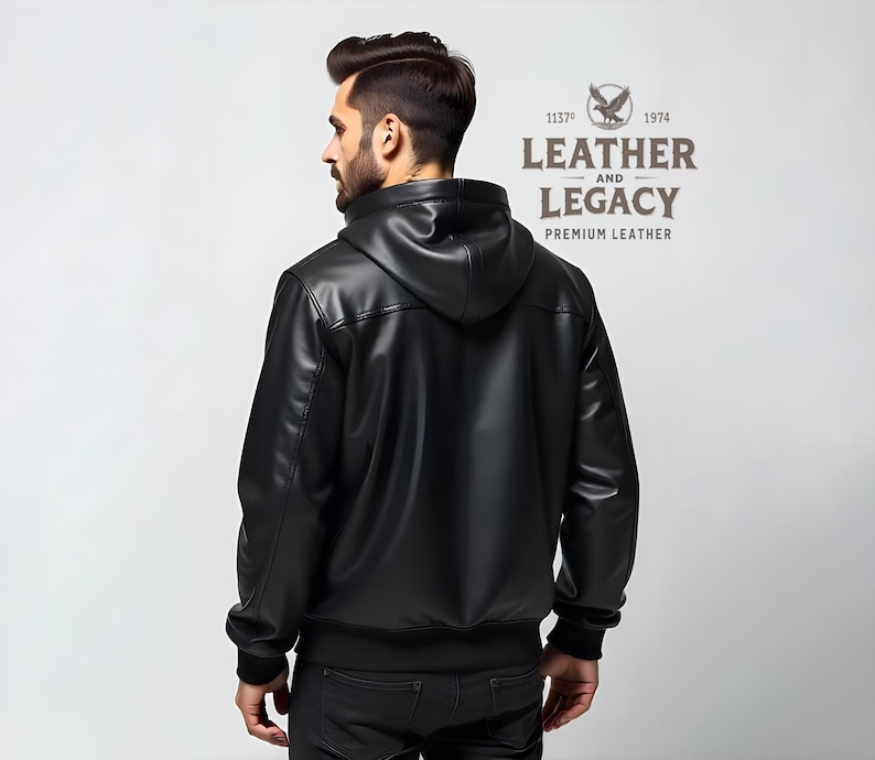 May include: Black leather jacket with a hood. The jacket has a zipper closure and a ribbed knit collar, cuffs, and waistband. The back of the jacket features a stitched detail. The jacket has the text "Leather and Legacy Premium Leather" on the back.