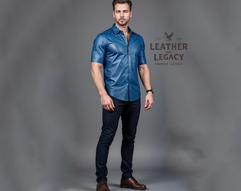 Può includere: Un uomo indossa una camicia di pelle blu a maniche corte e jeans blu scuro. La camicia ha un colletto abbottonato e una chiusura con bottoni. L'uomo è in piedi davanti a uno sfondo grigio. Il testo "Leather and Legacy Premium Leather" è visibile nell'immagine.