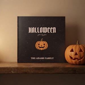 May include: A square black book with a textured surface featuring the white text HALLOWEEN year by year, a central orange jack-o'-lantern illustration, and the white text THE ADAMS FAMILY, accompanied by a carved orange pumpkin.