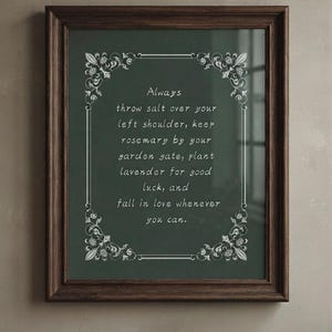 May include: A dark wood framed wall art piece featuring a deep green background with white decorative floral corner accents. The text reads: Always throw salt over your left shoulder, keep rosemary by your garden gate, plant lavender for good luck, and fall in love whenever you can.