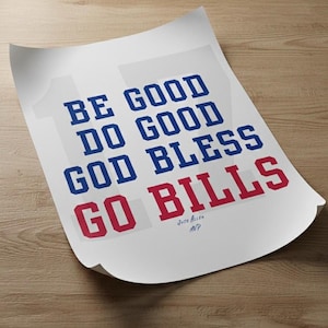 May include: A white poster with the text "BE GOOD DO GOOD GOD BLESS GO BILLS" in blue and red block letters. The poster is slightly curled and rests on a wooden surface. The text "Josh Allen MVP" is at the bottom.