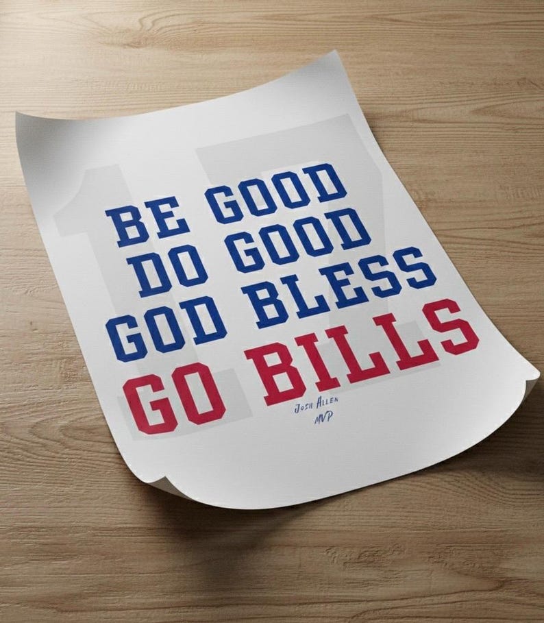 May include: A white poster with the text "BE GOOD DO GOOD GOD BLESS GO BILLS" in blue and red block letters. The poster is slightly curled and rests on a wooden surface. The text "Josh Allen MVP" is at the bottom.