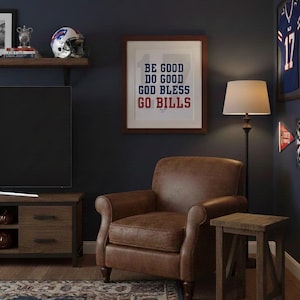 May include: A cozy living room with a brown leather armchair, a wooden side table, and a framed print that reads "BE GOOD DO GOOD GOD BLESS GO BILLS." A football helmet and jersey are also visible.