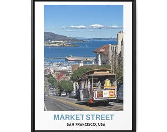 May include: A framed wall art print featuring a San Francisco cable car traveling down a street with a view of the bay and Alcatraz Island in the background. The text at the bottom reads MARKET STREET SAN FRANCISCO, USA in blue and black.