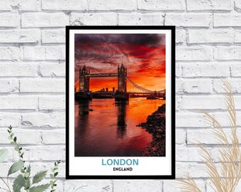 May include: A framed wall art print featuring a photograph of Tower Bridge in London at sunset with a vibrant red and orange sky. The print includes the text LONDON in blue and ENGLAND in black at the bottom against a white border.