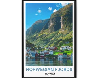 May include: A framed vertical wall art print featuring a landscape of the Norwegian Fjords with steep green mountains, a blue sky with clouds, and a small village of colorful houses along the water. The text reads NORWEGIAN FJORDS NORWAY.
