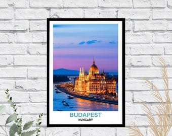 May include: A framed wall art print featuring a twilight view of the Hungarian Parliament Building in Budapest, illuminated in warm yellow light against a purple and blue sky, with the text BUDAPEST HUNGARY printed in blue and black below.