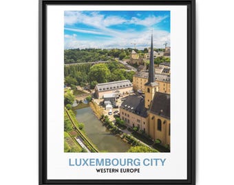 May include: A framed wall art print featuring a high-angle view of Luxembourg City, Western Europe. The image displays a river flowing past stone buildings with a tall church spire under a blue sky. The text reads LUXEMBOURG CITY WESTERN EUROPE.