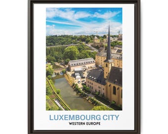 May include: A framed wall art print featuring an aerial view of Luxembourg City, Western Europe. The image displays a river flowing past stone buildings with a tall church spire under a blue sky. The text reads LUXEMBOURG CITY WESTERN EUROPE.