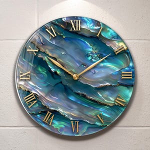 May include: A round wall clock featuring a vibrant blue and teal iridescent abalone shell pattern across the face. The clock has gold-coloured Roman numerals and matching gold-coloured hour and minute hands centred on the dial.