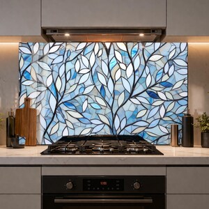 Könnte beinhalten: Eine dekorative Küchenrückwand mit einem Buntglasdesign eines Baumes mit blauen und weißen Blättern vor hellblauem Hintergrund. Die Rückwand ist über einem Gasherd und unter einer Dunstabzugshaube angebracht.