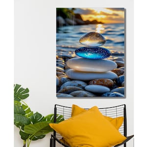 Pode incluir: Impressão emoldurada de uma cena de praia com uma pilha de pedras lisas e coloridas. A pedra superior é transparente, a do meio é azul e as outras são brancas. O fundo mostra um pôr do sol sobre o mar, com luz dourada.