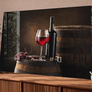 May include: A glass of red wine, a dark wine bottle, and a cluster of purple grapes resting on a wooden barrel. A larger wooden barrel stands behind the items. The scene is set against a dark, textured background with a window reflection.