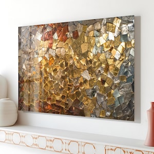 May include: Abstract wall art featuring a mosaic of irregular, reflective tiles in shades of gold, silver, and copper. The artwork is mounted on a white wall, creating a striking visual contrast. The tiles are arranged to create a textured, shimmering effect.