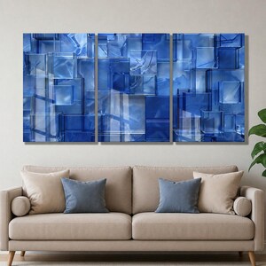Puede incluir: Una obra de arte mural tr&iacute;ptica con un dise&ntilde;o abstracto de bloques de vidrio azules superpuestos. La obra de arte tiene diferentes tonos de azul y blanco, creando una sensaci&oacute;n de profundidad. La obra de arte se exhibe sobre un sof&aacute; beige con cojines azules y beige.
