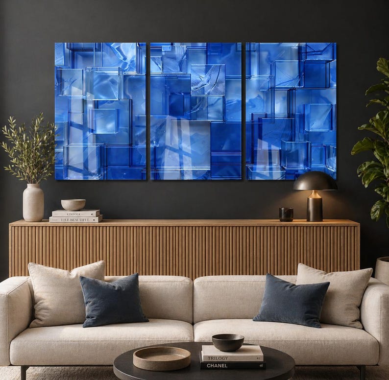 Puede incluir: Un tr&iacute;ptico de paneles de arte abstracto con un dise&ntilde;o geom&eacute;trico de bloques de vidrio azules. La obra de arte se exhibe sobre un mueble de madera, con un sof&aacute; beige y cojines azul oscuro en frente. Una l&aacute;mpara negra y objetos decorativos completan la escena.