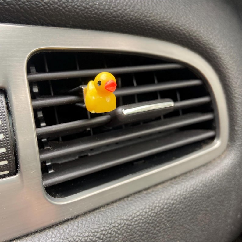 May include: A yellow rubber ducky car air freshener hanging from a car's air vent.