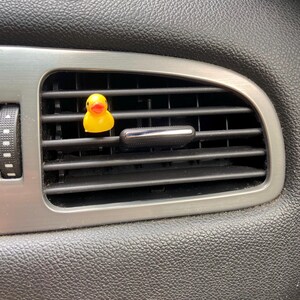 May include: A yellow rubber ducky air freshener hanging from a car's air vent.