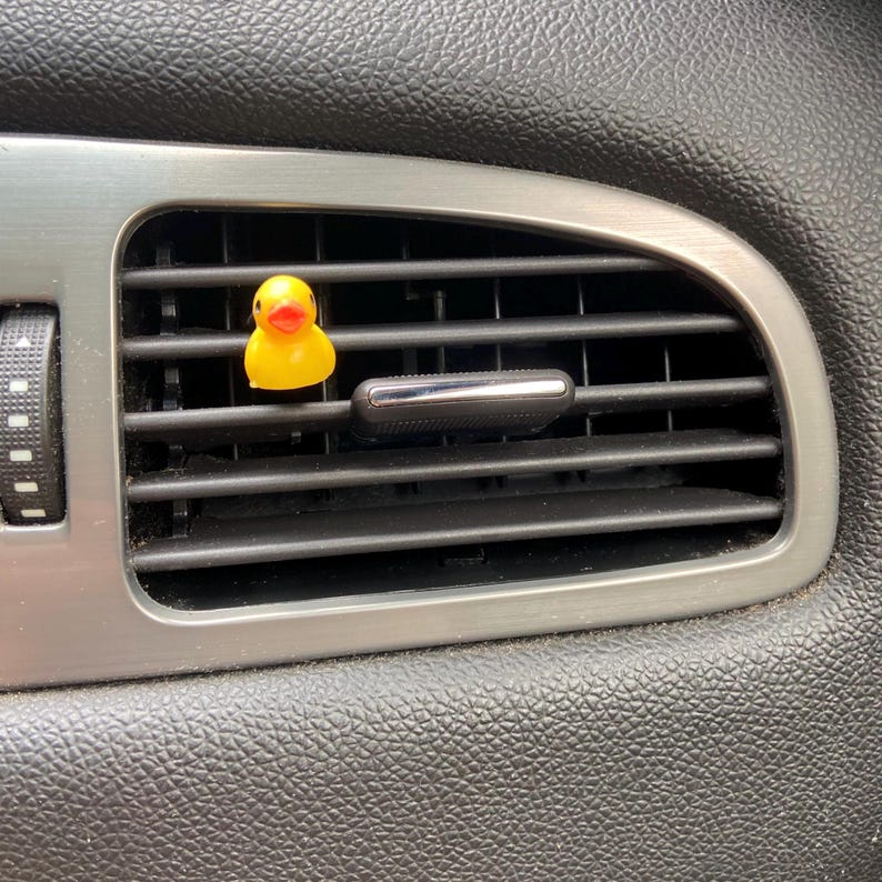 May include: A yellow rubber ducky air freshener hanging from a car's air vent.