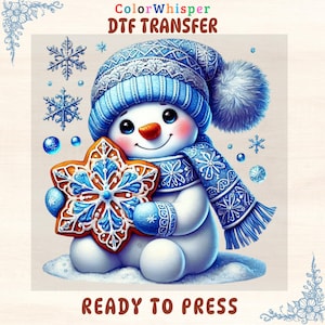 May include: A cheerful snowman wearing a blue hat, scarf, and mittens, holding a snowflake-shaped cookie. The snowman has a carrot nose and a smiling face. The image includes the text "ColorWhisper DTF TRANSFER" and "READY TO PRESS".