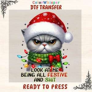 May include: A DTF transfer featuring a grumpy gray cat wearing a Santa hat and a green scarf with a red bow. The cat is adorned with Christmas lights. Text reads "LOOK AT ME BEING ALL FESTIVE AND SHIT READY TO PRESS."