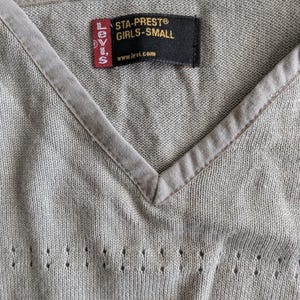 Peut inclure: Pull en tricot gris avec un col en V et une étiquette Levi's qui indique "Sta-Prest® Girls-Small www.levi.com".
