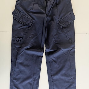 May include: Navy blue cargo pants with multiple pockets and a button closure. The pants have a relaxed fit and are made of a durable fabric. The design includes two large cargo pockets on the thighs and two smaller pockets.