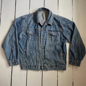 May include: A light blue denim jacket with a classic design. The jacket features a collared neckline, button-down closure, and multiple pockets. The sleeves have buttoned cuffs. The jacket is made of a sturdy denim material.